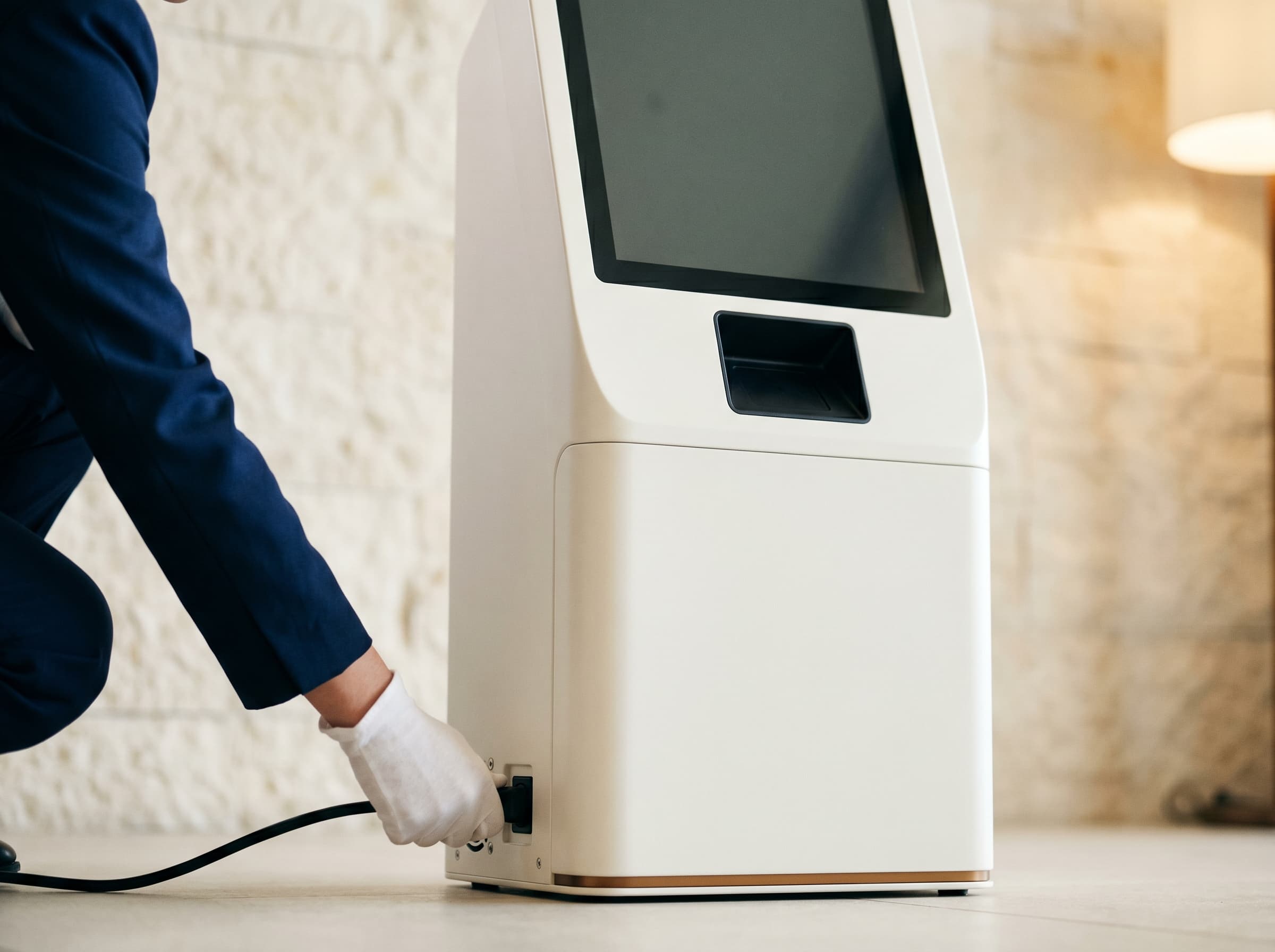 Hotelmitarbeiter steckt das Stromkabel in das ECG AI Terminal — Closeup mit ruhigem Lobbyhintergrund.